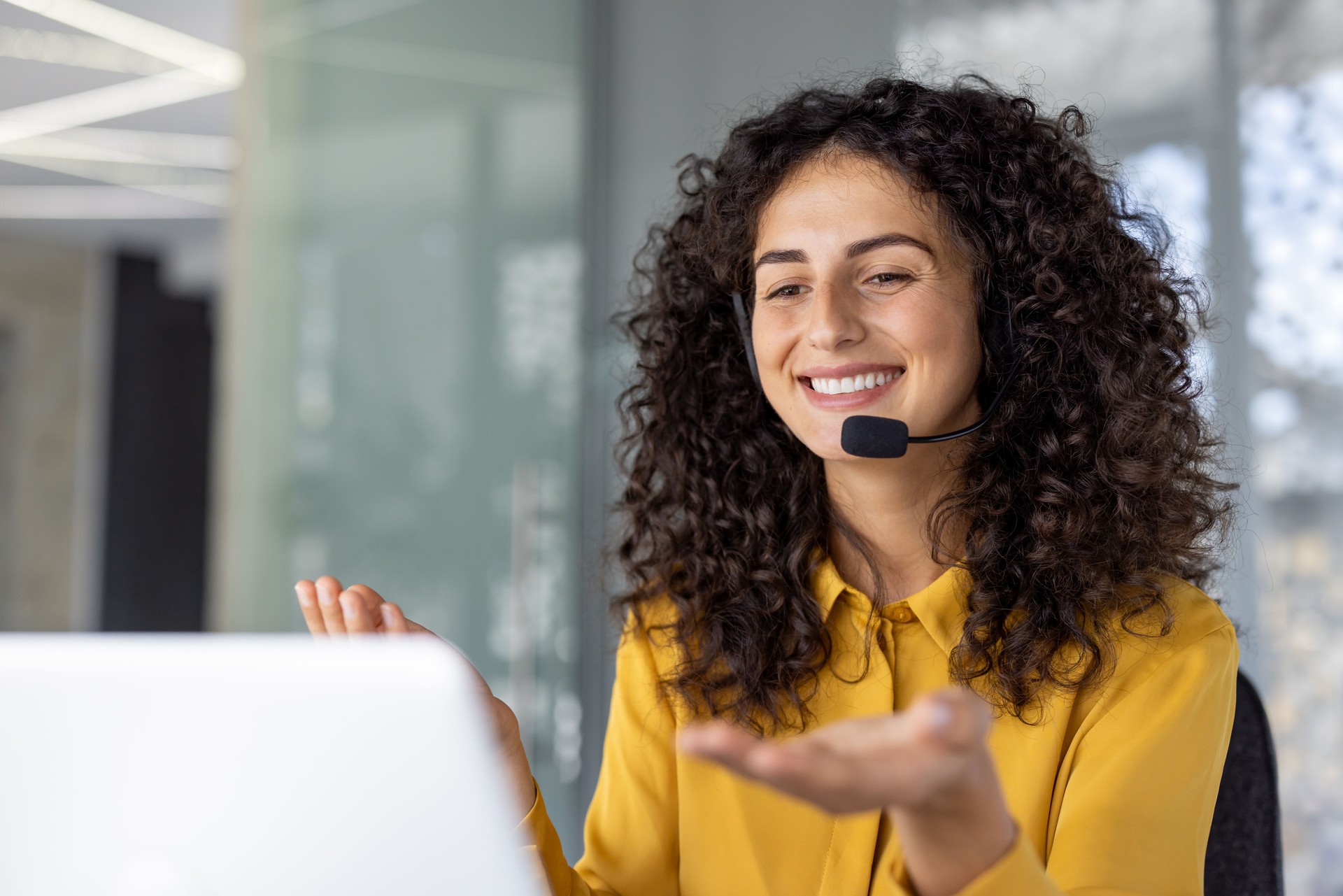 Hispanic businesswoman with curly hair smiling while working in modern office using headset for virtual meeting